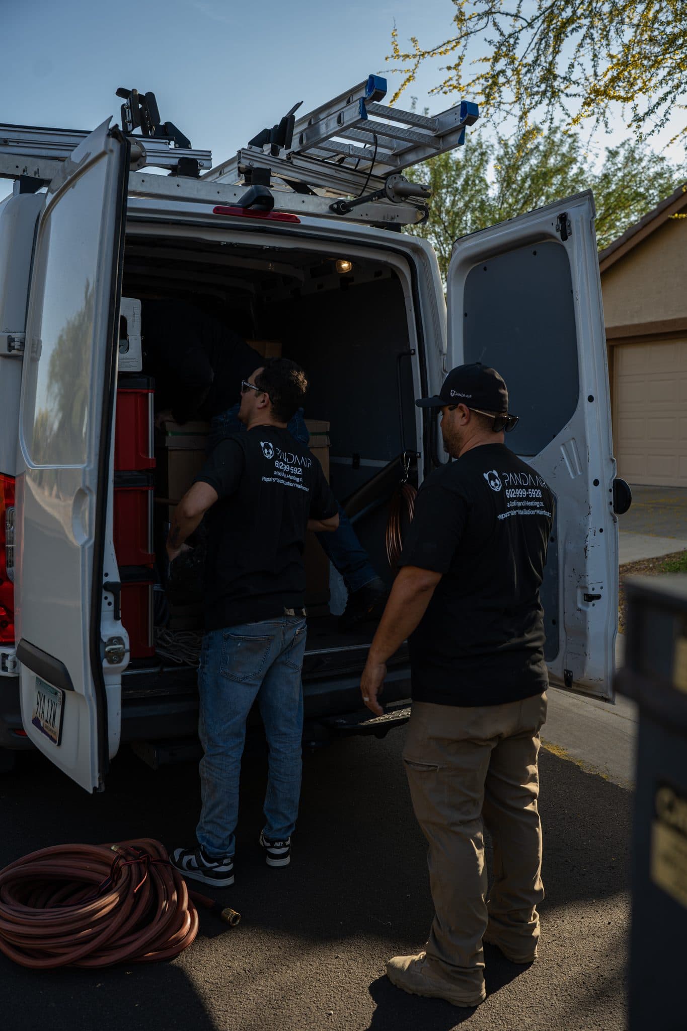 Two Panda Air technicians at the open rear doors of the service van in a driveway