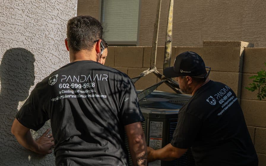 Two Panda Air technicians with their hands on a new condensing unit beside a block wall
